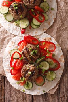 Grilled meat balls with fresh vegetables on a flat bread close up. Vertical top view
