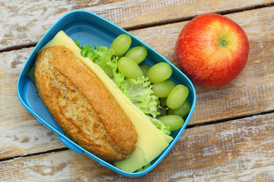 Healthy lunch box containing brown bread cheese sandwich, grapes and red apple

