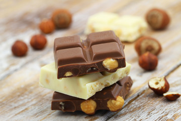 Milk and white chocolate pieces with whole hazelnuts stacked up on wooden surface
