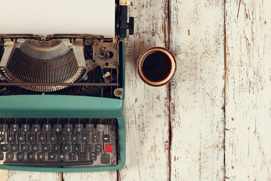 top view photo of vintage typewriter with blank page next to cup of coffee, on wooden table. retro filtered image
