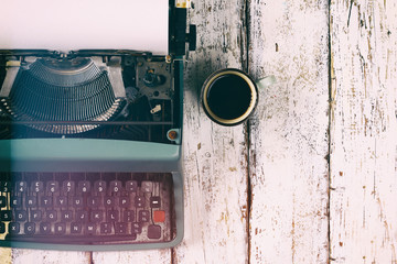 top view photo of vintage typewriter with blank page next to cup of coffee, on wooden table. retro filtered image
