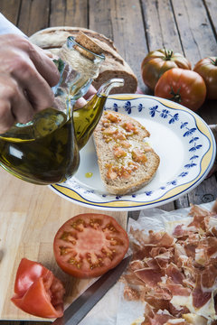 Chef que se dispone a verter aceite de oliva sobre una tostada de pan con tomate, ajo y jamón.