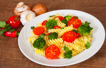 Fusilli pasta with cherry tomatoes and broccoli in a plate on wooden table