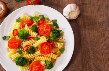Fusilli pasta with cherry tomatoes and broccoli in a plate on wooden table