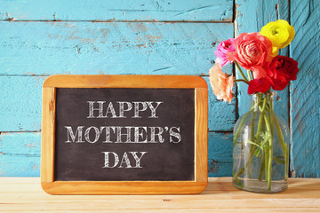 flowers next to blackboard on wooden table. happy mother's day concept. vintage filtered
