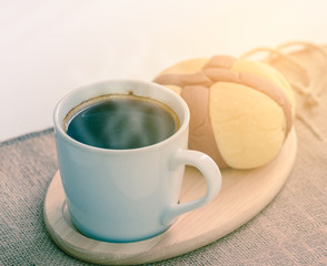 Hot coffee and bread on wooden coaster.