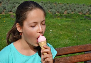 young girl sitting on a park bench and licking ice cream