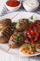 Kofte kebab with grilled vegetables on a plate and sauce close-u
