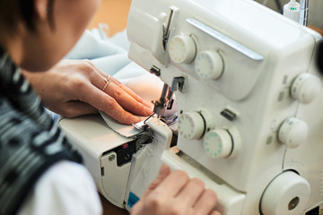 A seamstress sews clothes sitting on the sewing machine in the workshop