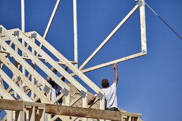 Man reaching high for roof truss with carpenter building crew - obrazy, fototapety, plakaty