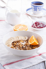 Homemade granola with fresh fruits in a white bowl with jam, milk and coffee on a wooden background for breakfast, closeup.