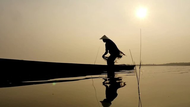 Silhouette of traditional fishermen throwing net fishing in the lake at sunrise time