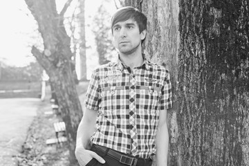 Man standing by a tree in a plaid shirt and rays of the sun