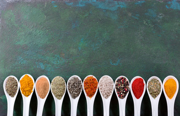 various spices in spoons on old green background