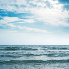 waving sea and cloudy sky with sun over it