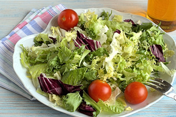 Fresh lettuce and cherry tomatoes .   Leaves of fresh lettuce and cherry tomatoes on a white dish on a blue wooden background.