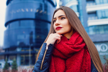 Fashion shot of pretty young woman over city background, wearing red scarf. City lifestyle. Female fashion