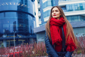 Fashion shot of pretty young woman over city background, wearing red scarf. City lifestyle. Female fashion