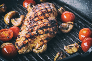 Grilled chicken breast in different variations with cherry tomatoes, .mushrooms, herbs, cut lemon on a wooden board or teflon pan. Traditional cuisine. Grill kitchen.