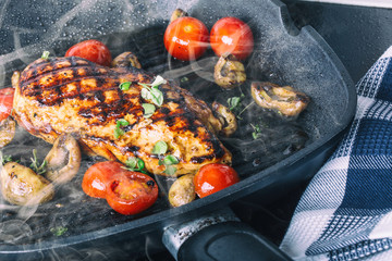 Grilled chicken breast in different variations with cherry tomatoes, .mushrooms, herbs, cut lemon on a wooden board or teflon pan. Traditional cuisine. Grill kitchen.