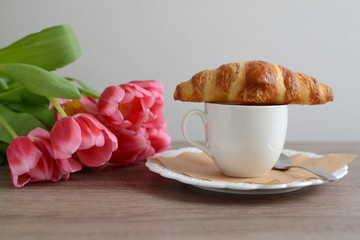 cup of cappuccino and yummy croissant with flowers