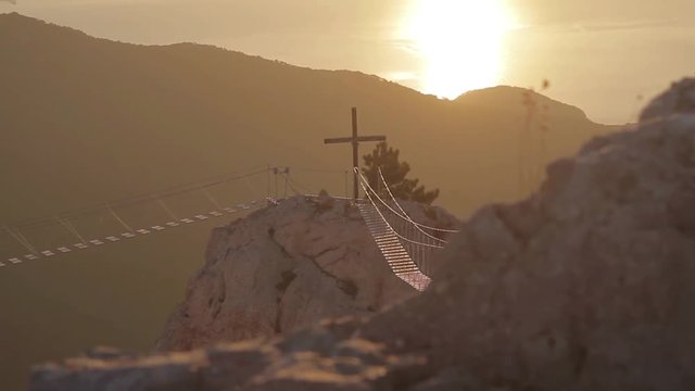  View of the catholic cross and rope ladder over the abyss. Crimea, Ukraine.Ayu Dag Mountain view from the top of Ai Petri mountain during sunrise. Handheld shot, rack focus.