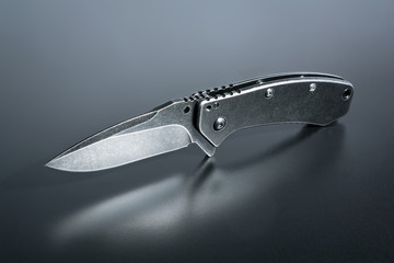 An Opened Black Folding Knife Standing On Dark Ground With Reflection