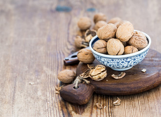 Walnuts in ceramic bowl and on cutting board with nutcracker over  rustic wooden background