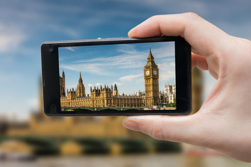 Tourist holds smartphone in hand and photographing Big Ben in London.