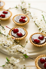Mini tarts with chocolate and cherries decorated cherry blossom on white wooden background. Selective focus