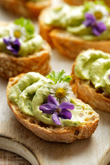 Obraz na płótnie Canvas Sandwiches with avocado paste with the addition of edible flowers violets and daisies