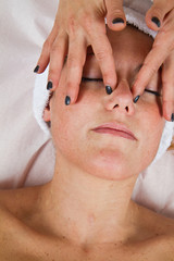 Beautiful young woman receiving facial massage with closed eyes