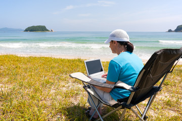 Middle-aged woman uses a laptop while on the beach