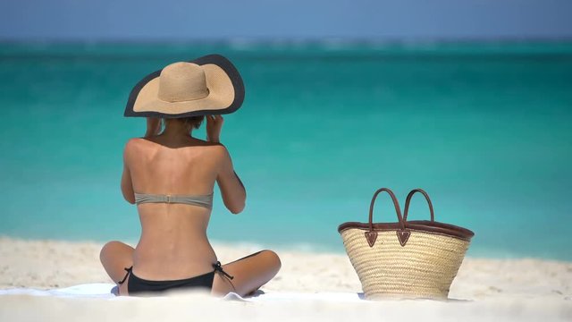 Sexy bikini woman tanning relaxing on beach. Suntan concept. Unrecognizable female adult from the back lying down with straw hat sunbathing under the tropical sun on Caribbean vacation.