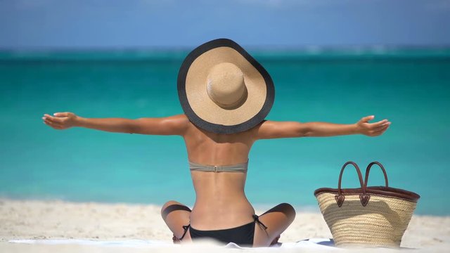 Summer Vacation. Happy serene joyful young woman on beach in bikini arms outstretched looking at ocean. Pretty female is sunbathing during vacation. Lady is enjoying summertime against turquoise sea.