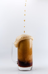 Pouring process of dark stout beer into a beer glass mug, splashes, drops and froth around glass mug