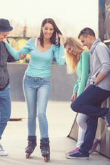 Group of teenagers having fun in a skate park  helping their friend to learn to roller skate