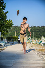 Young man standing at the beach throwing loafer