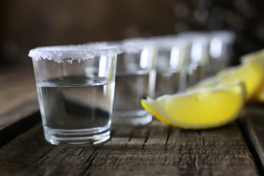 stack of tequila with salt and lemon on a wooden background