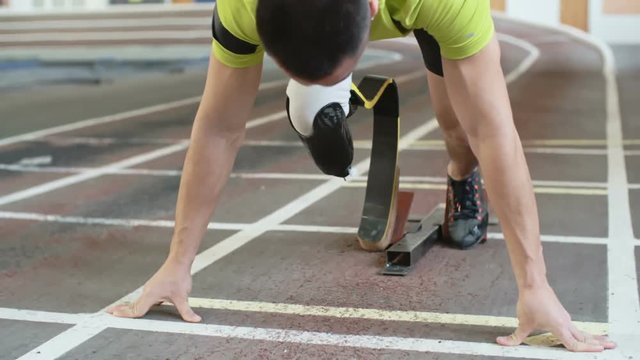 Young athlete with artificial leg starting from blocks on track in slow motion