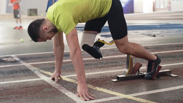 Slow motion shot of determined athlete with prosthetic leg starting from blocks on track