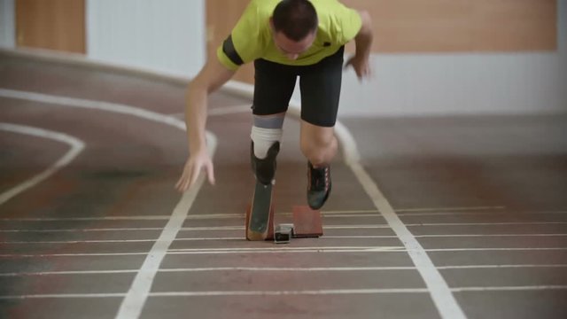 Young determined amputee athlete with artificial leg starting from blocks and running towards the camera in slow motion  