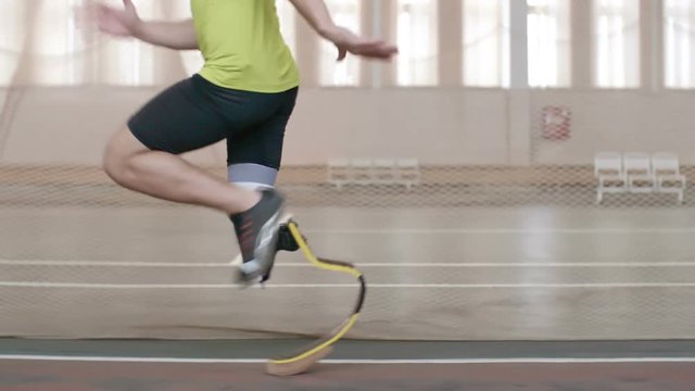 Tracking shot of Paralympic athlete with prosthetic leg running on track in slow motion 