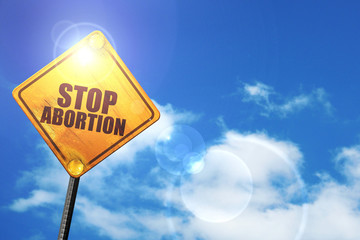Yellow road sign with a blue sky and white clouds: stop abortion