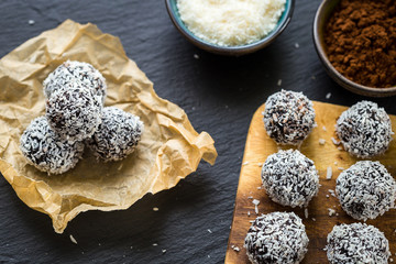 Homemade Healthy Paleo Raw Chocolate Truffles with Nuts, Dates and Coconut Flakes on Dark Background