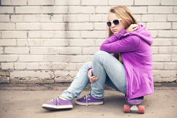 Blond girl in sunglasses sits on her skateboard