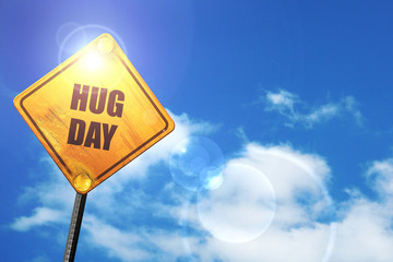 Yellow road sign with a blue sky and white clouds: hug day