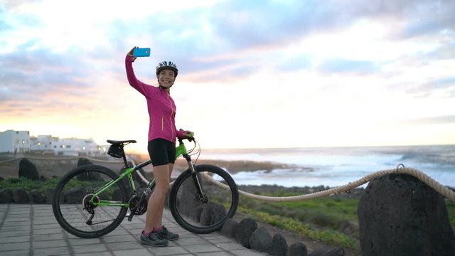 Mountain biking MTB cyclist woman cycling on bike relaxing taking selfie with smart phone at sunset view. Female mountain biker enjoying healthy active lifestyle on Lanzarote, Canary Islands, Spain