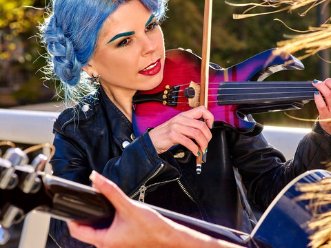 Music street performers girl with blue hair violinist  playing  aganist sky with clouds outdoor. The second girl - violinist with her.
