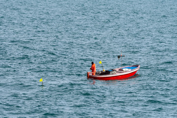 Fisherman on a small red fishing boat between the waves of the sea. Liguria, Italy